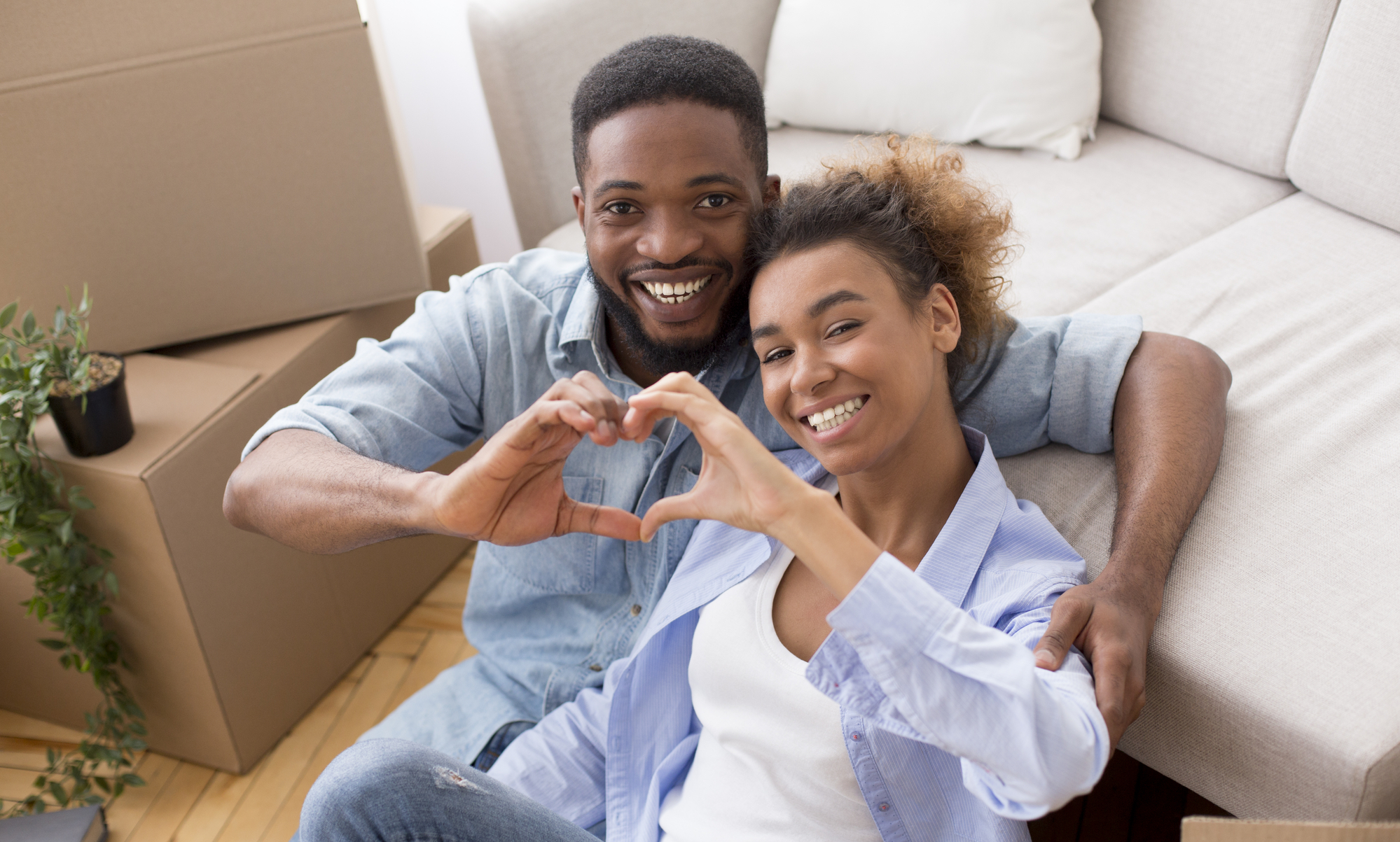 Afro Spouses Gesturing Heart Shape Hugging Among Moving Boxes Indoor