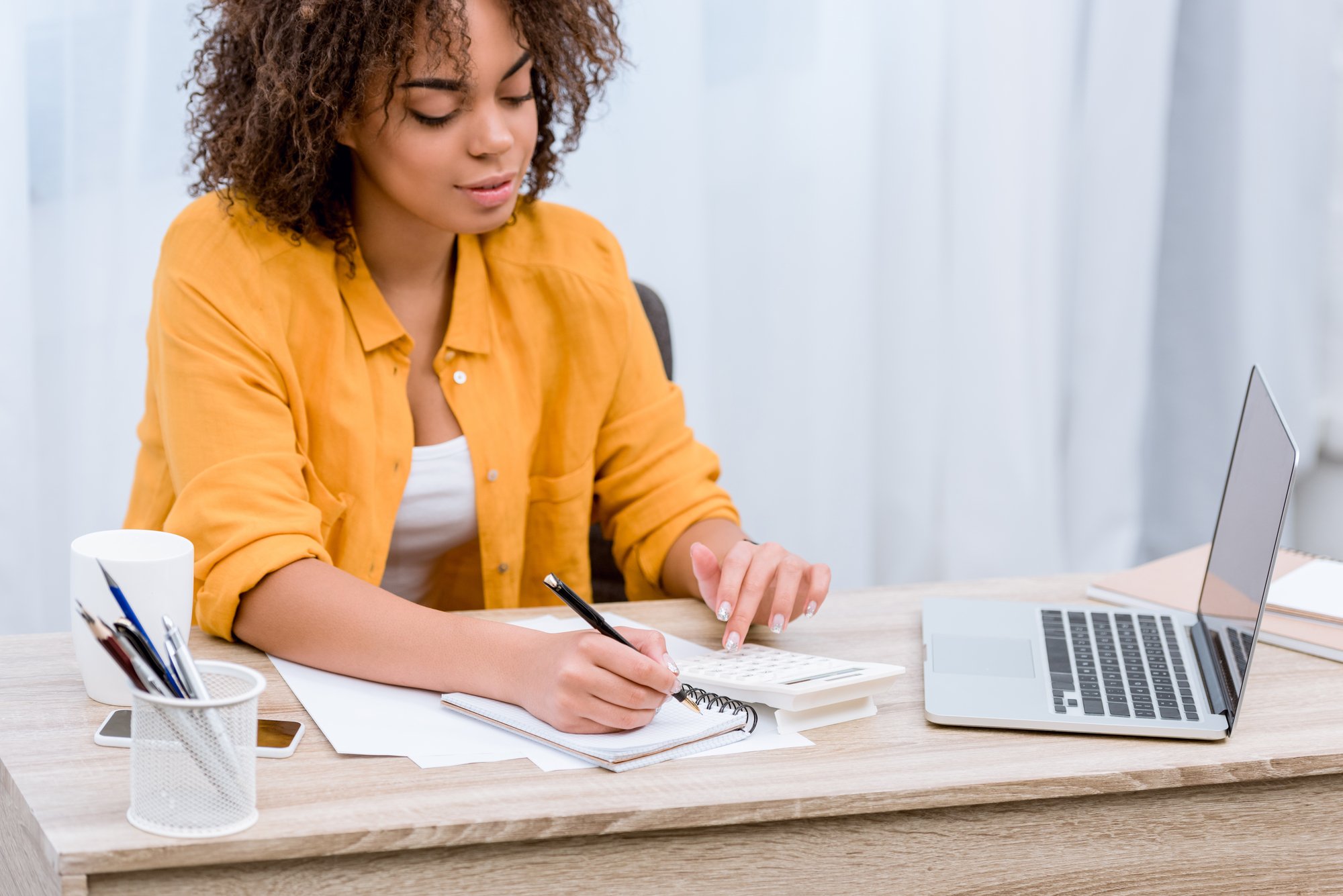 Beautiful young woman working with laptop and writing in notebook